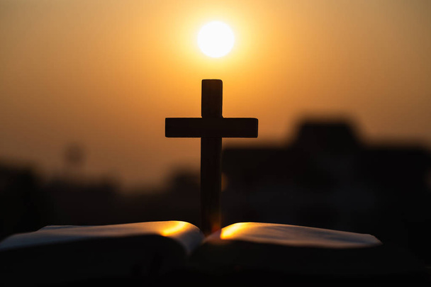 Silhouette of  wooden Christian cross on bible with a bright sun - Photo, Image