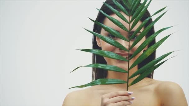 Beautiful young woman with perfect skin and natural makeup posing front of a plant. Tropical green leaves background with fern. SPA, wellness, bodycare and skincare. - Filmagem, Vídeo