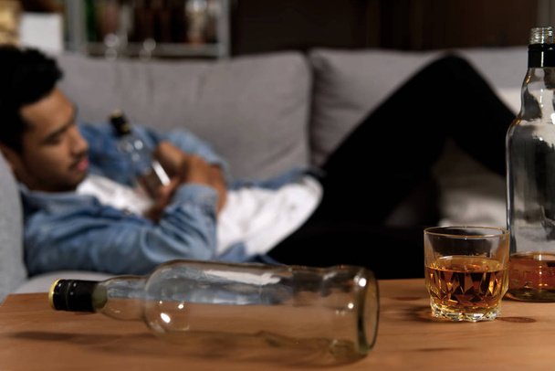 酔っぱらいソファーで寝ていると 1 泊でアルコールをたくさん飲んだ後にウイスキーのボトルを保持しています。ボトルとグラスはどのくらい飲んだかを示す表に置くのいくつか。アルコール依存症の概念. - 写真・画像
