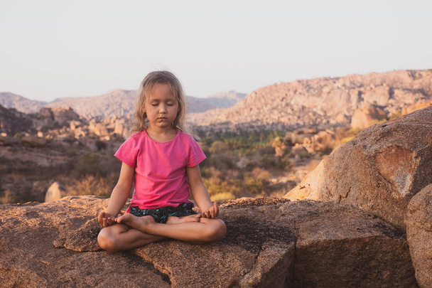 Little cute girl meditating on top of mountain. - Valokuva, kuva