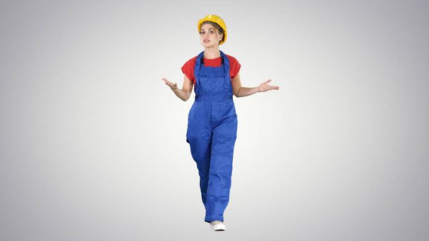 Cheerful female construction worker talking to camera on gradient background. - Zdjęcie, obraz