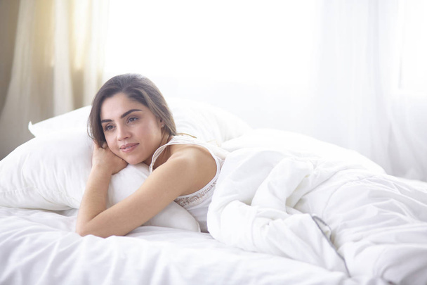 beautiful young woman basking in bed in the morning. Beautiful Model face looks sexy in camera - Foto, afbeelding