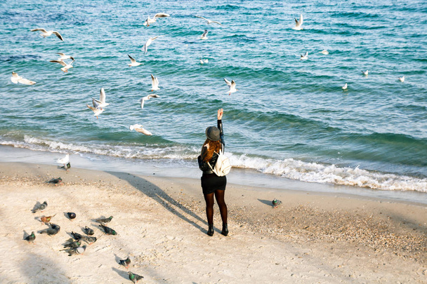 kobieta nie do poznania w kapelusz jest karmienie mewy i gołębie na brzegu morza - Zdjęcie, obraz