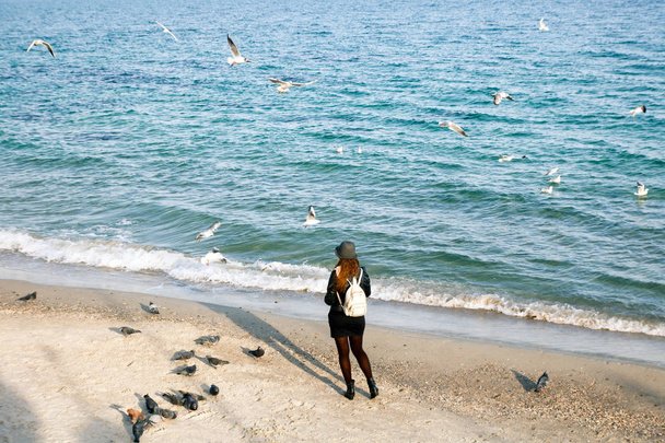 Unerkennbares Weibchen mit Hut füttert Möwen und Tauben am Meeresstrand - Foto, Bild