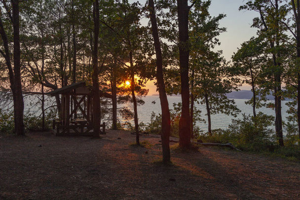 schöne Landschaft bei Sonnenuntergang mit Bäumen und blauem Meer. Holzlaube unter den Eichen, Sommercampingplatz am Abend. Hintergrund Natur. - Foto, Bild