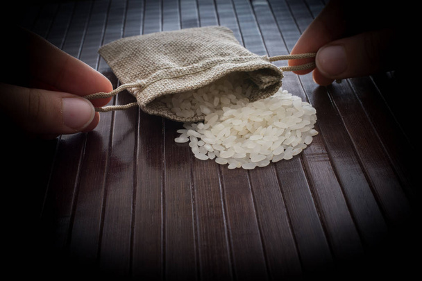 Hand holding straw pouch full of uncooked rice on wooden backgro - Фото, изображение