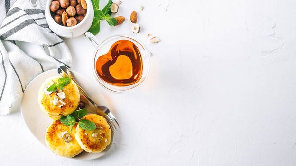 Aamiainen tai lounas käsite. Raejuustopannukakkuja hunajalla, pähkinöillä ja mintulla valkoisella taustalla. Ylhäällä näkymä, bannerin kuva - Valokuva, kuva