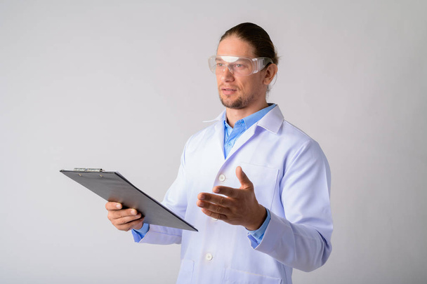 Hombre médico con gafas protectoras hablando mientras sostiene el portapapeles
 - Foto, imagen