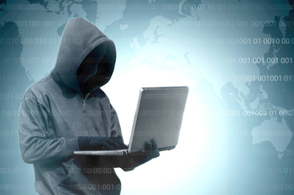 Hacker in black hoodie holding laptop with binary code on virtua - Zdjęcie, obraz