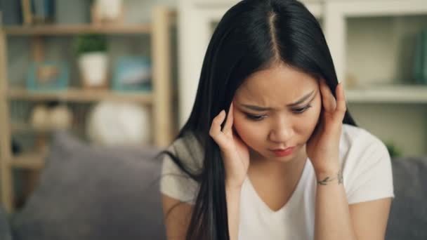 Unhappy Asian female student is feeling bad having headache and trying to release pain massaging her head touching temples with sad face. Sick youth concept. - Materiał filmowy, wideo