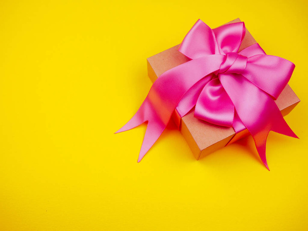 ajándékdoboz rózsaszín szatén szalaggal sárga háttérrel - Fotó, kép