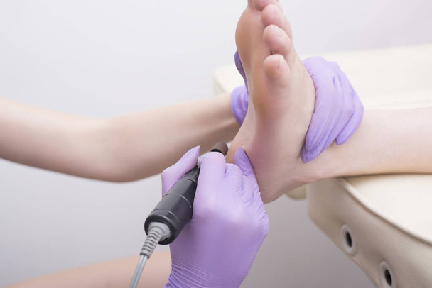 Fußhautbehandlung. behandschuhte Hände mit einem Pediküre-Gerät. Nahaufnahme - Foto, Bild