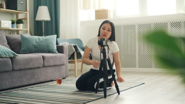 Ελκυστική Ασίας blogger εγκατάσταση κάμερας στο τρίποδο και προσαρμογή εξοπλισμού στη συνέχεια κάθεται στο πάτωμα και εγγραφή βίντεο για online vlog. Τεχνολογία και τον τρόπο ζωής έννοια. - Πλάνα, βίντεο