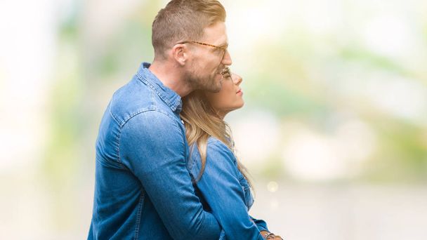 Jeune couple amoureux portant des lunettes sur fond isolé regardant vers le côté, pose de profil relax avec visage naturel avec sourire confiant
. - Photo, image