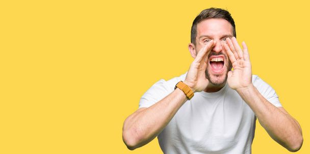 Красивый мужчина в обычной белой футболке кричит сердито с руками над ртом
 - Фото, изображение