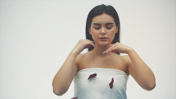 Beautiful brunette girl in her beauty. A golden evening makeup and a red lipstick with dark hair on a white background. the petals of red roses flying up to her face. - Metraje, vídeo