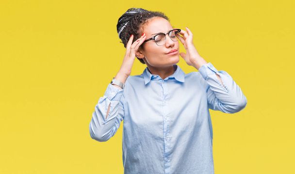Jeune fille d'affaires afro-américaine cheveux tressés portant des lunettes sur fond isolé avec la main sur la tête pour la douleur à la tête parce que le stress. Migraine souffrante
. - Photo, image