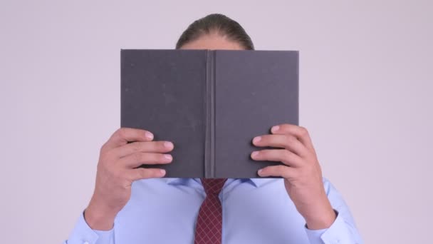 Face of shy businessman thinking while covering face with book - Filmmaterial, Video