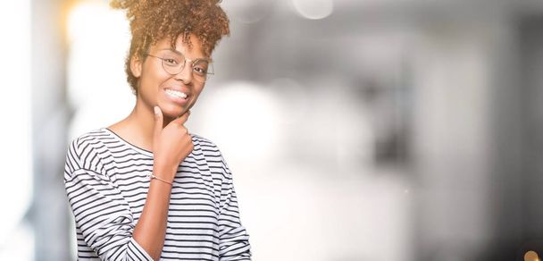 Krásná mladá africká americká žena nosí brýle izolované pozadí sebevědomým na kameru s úsměvem se zkříženýma rukama a ruku a na bradě. Pozitivní myšlení. - Fotografie, Obrázek
