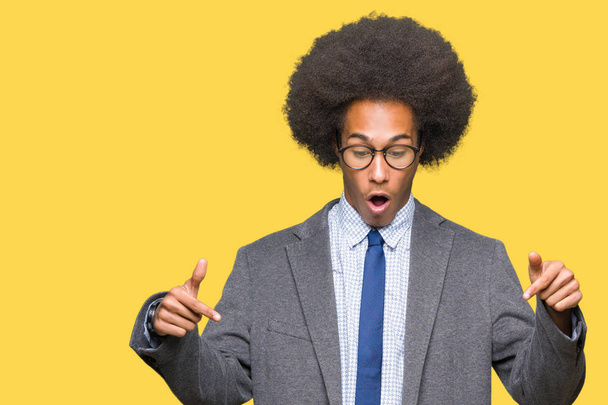 Joven hombre de negocios afroamericano con cabello afro usando gafas Señalando con los dedos mostrando publicidad, cara sorprendida y boca abierta
 - Foto, imagen