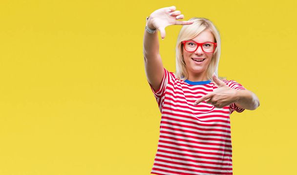 Young beautiful blonde woman wearing glasses over isolated background smiling making frame with hands and fingers with happy face. Creativity and photography concept. - Photo, image