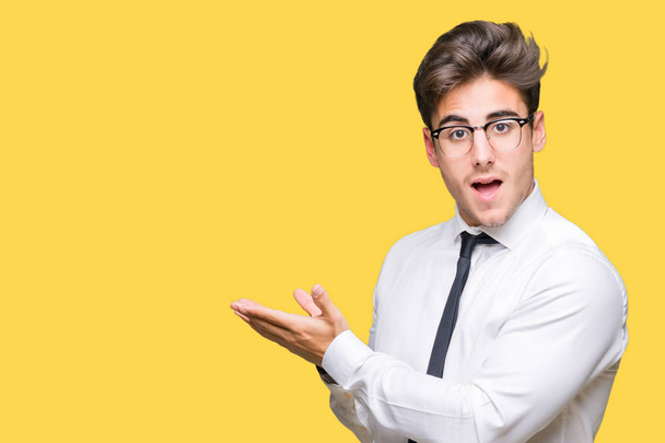 Young business man wearing glasses over isolated background Pointing to the side with hand and open palm, presenting ad smiling happy and confident - Photo, Image