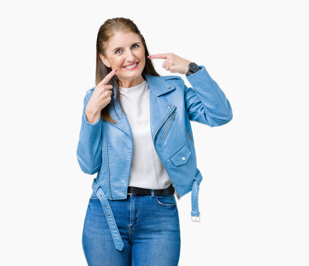 Beautiful middle age mature woman wearing fashion leather jacket over isolated background smiling confident showing and pointing with fingers teeth and mouth. Health concept. - Valokuva, kuva