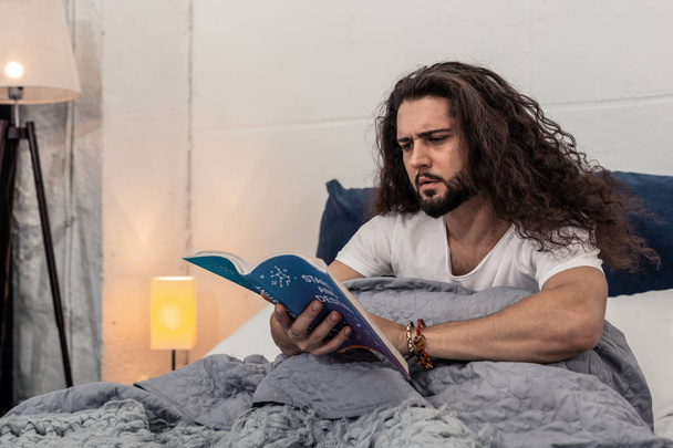 Serious young man reading a book on astrology - Fotó, kép