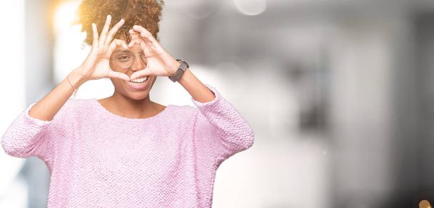 Beautiful young african american woman wearing glasses over isolated background Doing heart shape with hand and fingers smiling looking through sign - Φωτογραφία, εικόνα