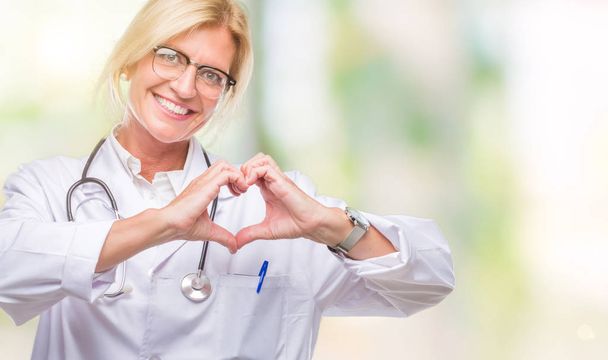 Middle age blonde doctor woman over isolated background smiling in love showing heart symbol and shape with hands. Romantic concept. - Foto, Imagem
