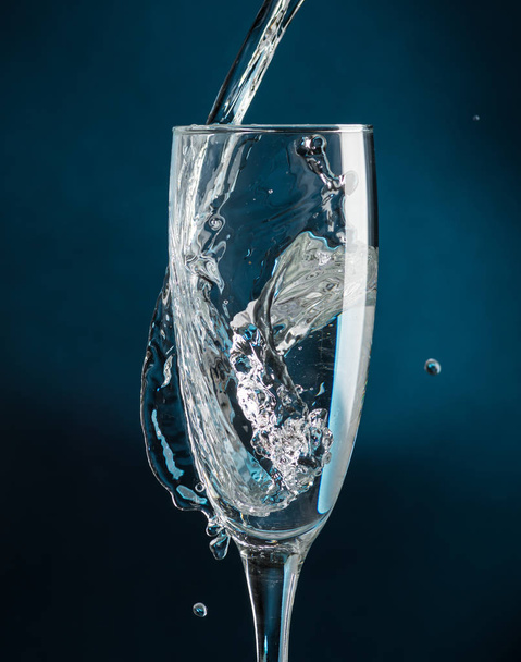 Spritzen im Champagnerglas gegen fallendes Wasser auf dunkelblauem Hintergrund - Foto, Bild
