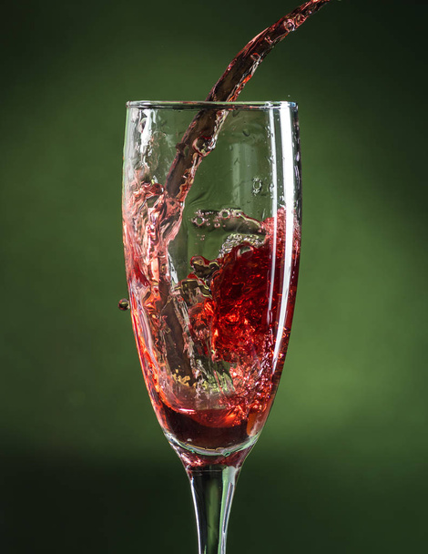splash in wine glass from falling red wine on a dark green background - Foto, Bild