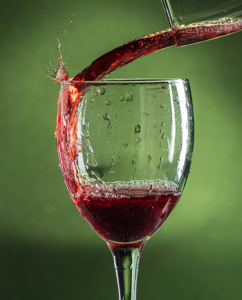 splash in wine glass from falling red wine on a dark green background - Foto, Bild