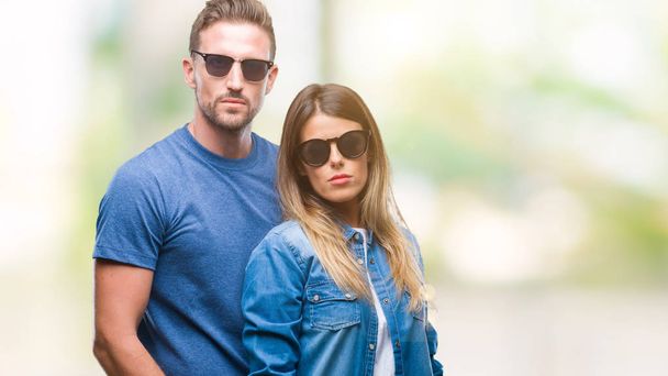 Young couple in love wearing sunglasses over isolated background with serious expression on face. Simple and natural looking at the camera. - Photo, Image