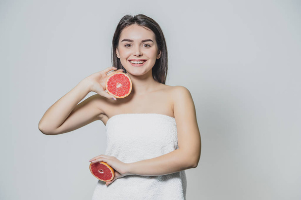 Beauty portrait of a beautiful healthy young topless woman with long red hair showing sliced grapefruit. Isolated over grey background. - Foto, Imagen