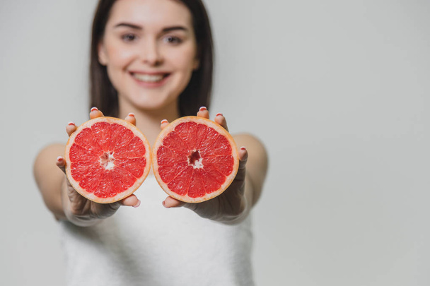 Young sexy girl posing with slices of red grapefruit in her arms extended forward. On a gray background. - Valokuva, kuva