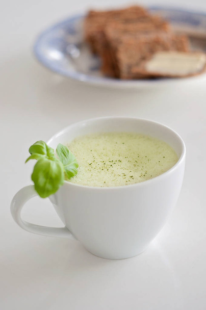 Té verde saludable con leche de soja y avena en una taza de té blanco decorado con albahaca y espuma en la parte superior - una bebida caliente para mejorar la función cerebral y como prevención del cáncer! Pan crujiente y mantequilla borrosa en el fondo
 - Foto, Imagen