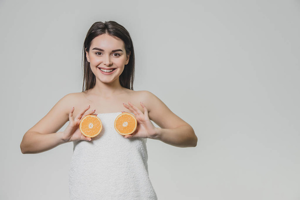 Happy young girl posing with fruits. Fragments of an orange in hands on a white background. Lifting the arms to the level of the chest, two pieces of fruit are kept. - Фото, изображение