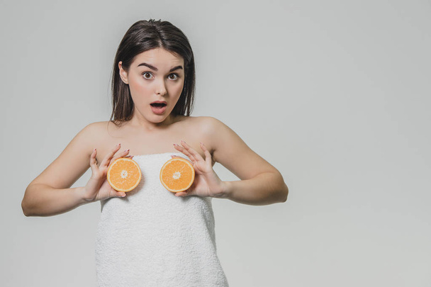 Happy young girl posing with fruits. Fragments of an orange in hands on a white background. Lifting the arms to the level of the chest, two pieces of fruit are kept. - Fotó, kép