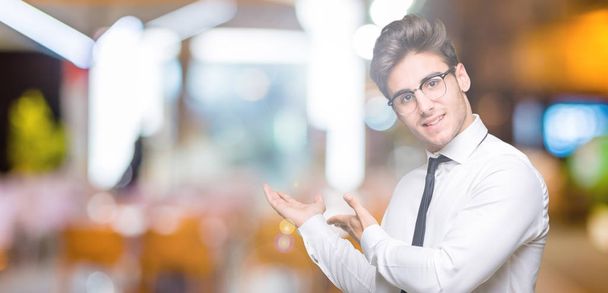 Jonge zakenman bril over geïsoleerde achtergrond uitnodigen om glimlachen natuurlijke met open hand - Foto, afbeelding