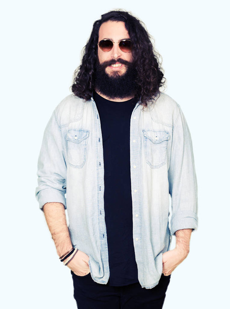 Young hipster man with long hair and beard wearing sunglasses with a happy and cool smile on face. Lucky person. - Photo, Image