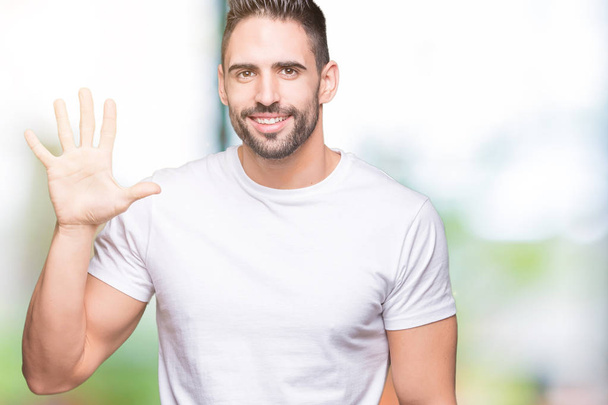Young man wearing casual white t-shirt over isolated background showing and pointing up with fingers number five while smiling confident and happy. - Фото, изображение