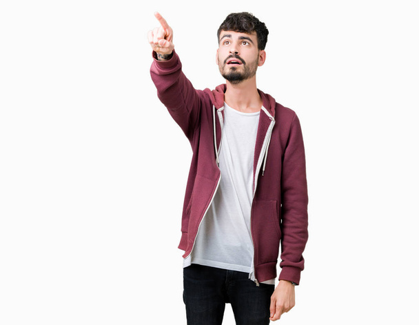 Young handsome man over isolated background Pointing with finger surprised ahead, open mouth amazed expression, something in front - Photo, Image