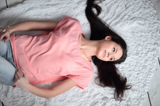junge Frau liegt auf weißem Teppich im Wohnzimmer - Foto, Bild