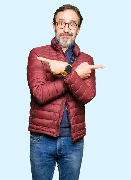 gutaussehender Mann mittleren Alters mit Brille und Wintermantel, der mit den Fingern nach beiden Seiten zeigt, unterschiedliche Richtung - Foto, Bild