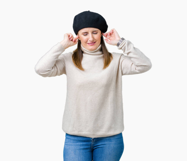 中年熟女の大声で音楽の音の腹が立つ式の指を使って耳をカバー分離の背景に冬セーター、ベレー帽身に着けています。聴覚障害者の概念. - 写真・画像