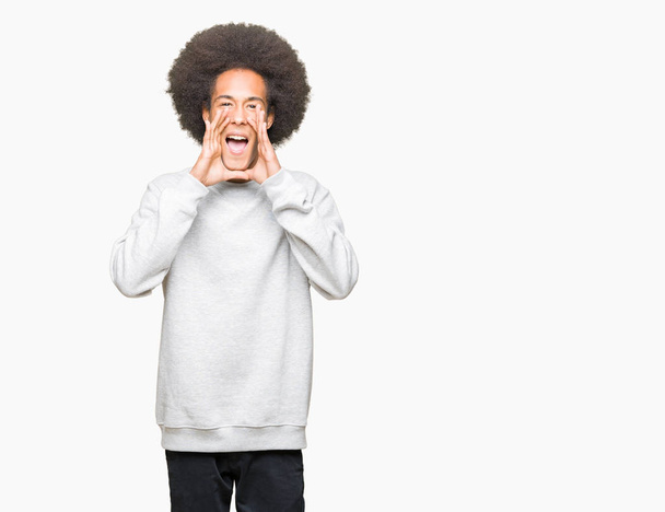 Giovane uomo afro americano con i capelli afro indossa felpa sportiva urlando arrabbiato ad alta voce con le mani sulla bocca
 - Foto, immagini