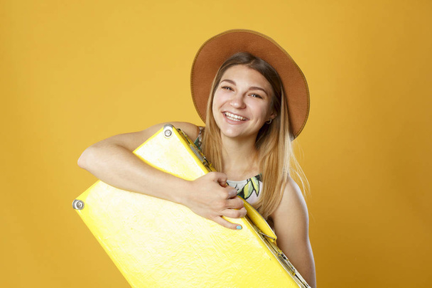 Happy tourist woman holding travel yellow case and credit card. Studio portrait. Vacation concept. - Фото, зображення