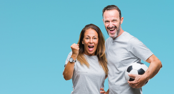 Middle age hispanic couple holding football soccer ball over isolated background screaming proud and celebrating victory and success very excited, cheering emotion - Fotografie, Obrázek