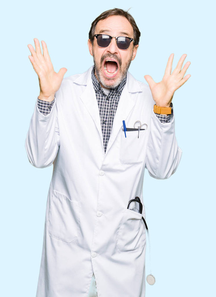 Красивий середнього віку лікар чоловік в сонцезахисних окулярах святкує божевілля і вражений успіхом з піднятими руками і відкритими очима кричить схвильовано. концепція переможця
 - Фото, зображення
